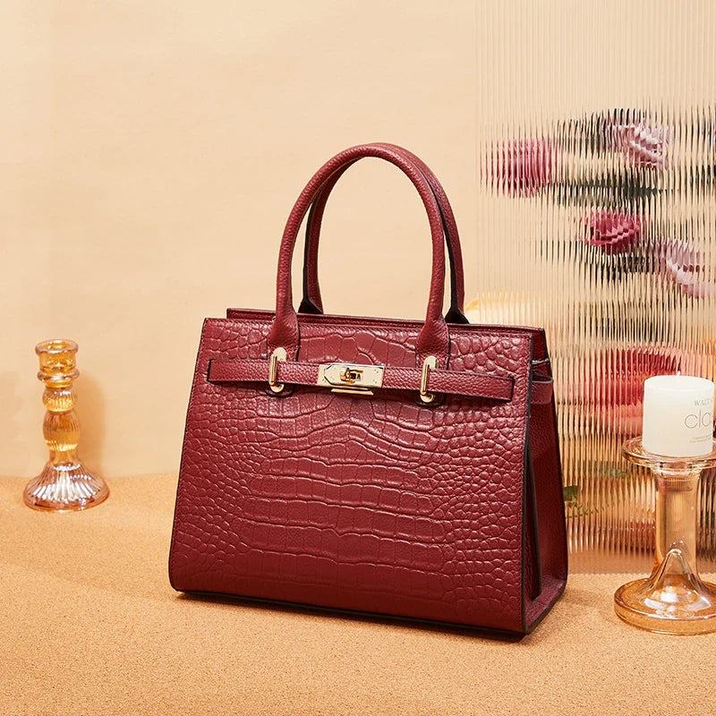 Burgundy handbag with a crocodile-style surface pattern and gold-tone hardware on a warm beige display.