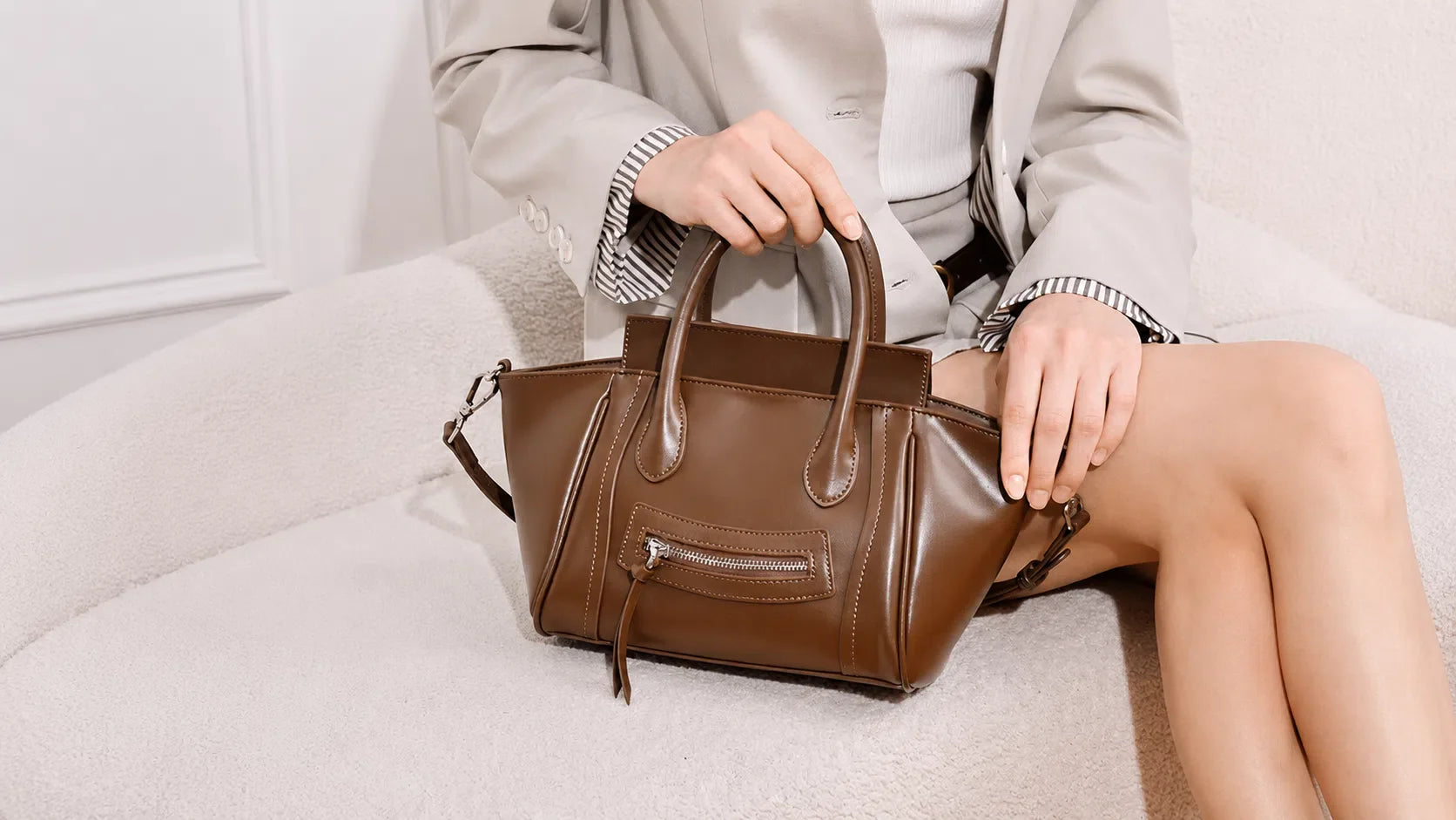 Cuirae brown genuine leather curved wing handbag with front zipper, structured handles, and polished stitching in a lifestyle close-up.