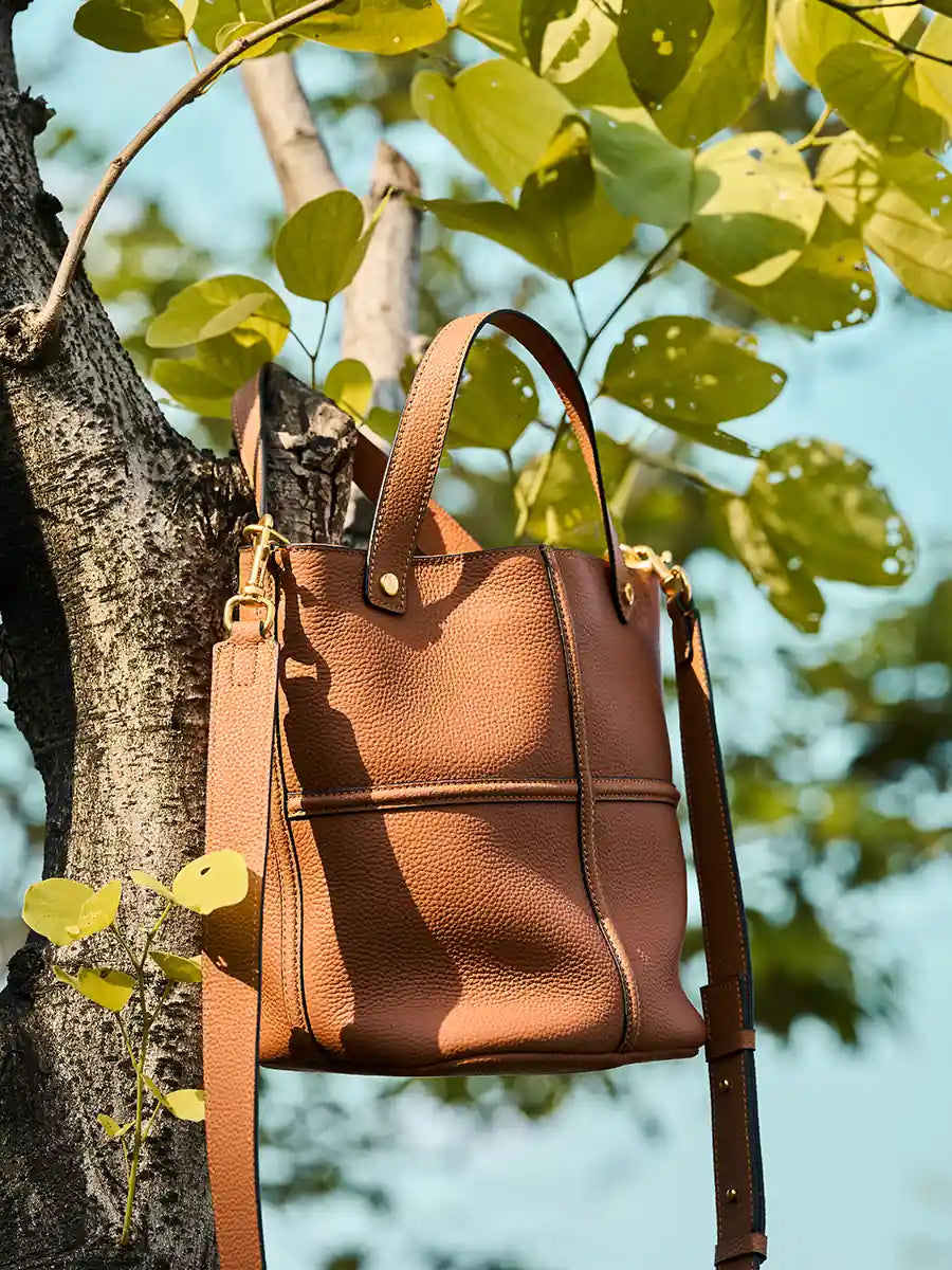 Brown Cuirae leather bucket bag hanging beside a tree outdoors