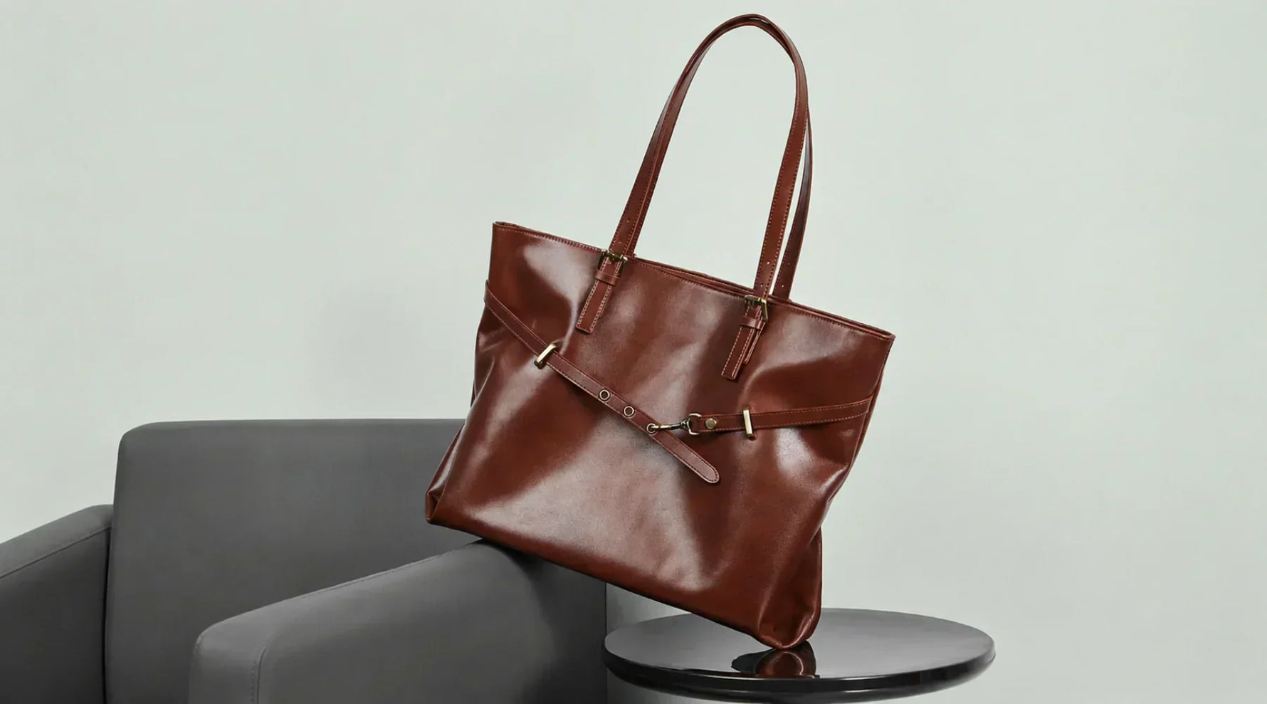 A coffee genuine leather handbag by Cuirae resting on a grey chair.