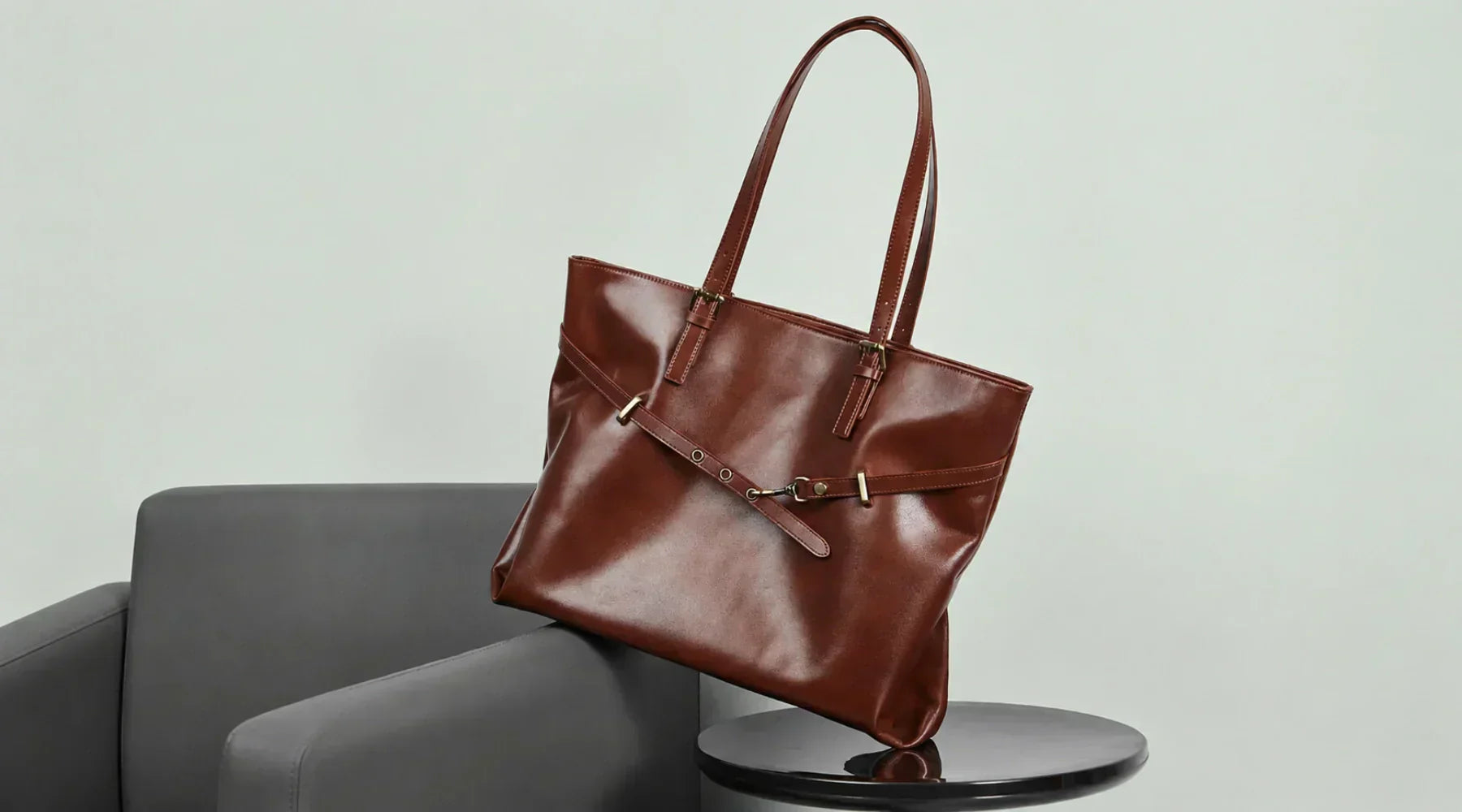 A coffee genuine leather handbag by Cuirae resting on a grey chair.
