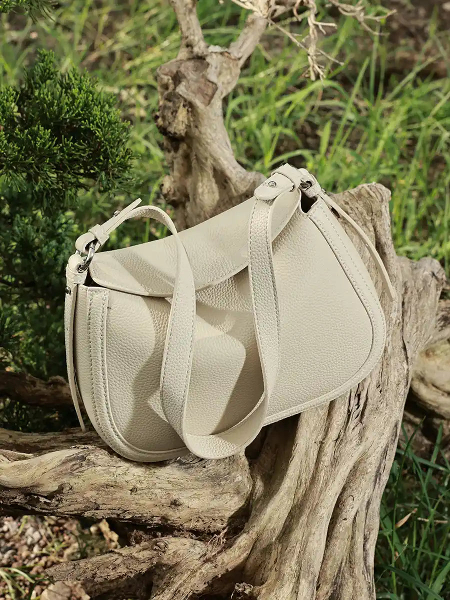 Ivory Cuirae pebbled leather flap shoulder bag resting on a tree trunk outdoors