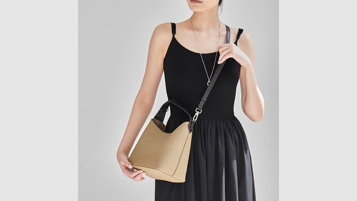 Woman wearing a tan leather bucket bag crossbody to show everyday size and strap placement