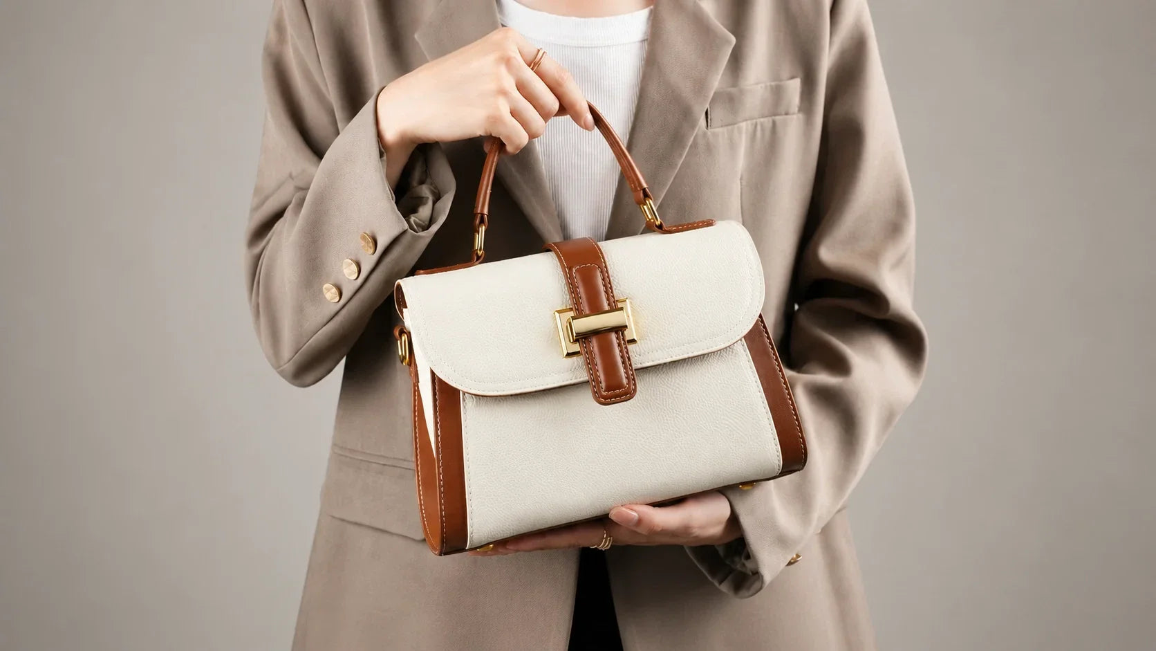 Woman holding a cream and brown leather shoulder bag with a structured flap and top handle