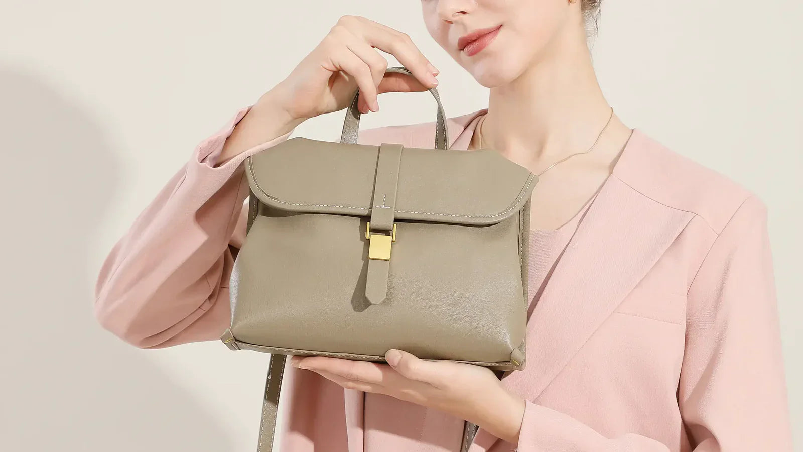 Cuirae taupe genuine leather handbag with gold buckle hardware, handheld by model in natural light, 16:9 cover for lightweight leather travel tote guide