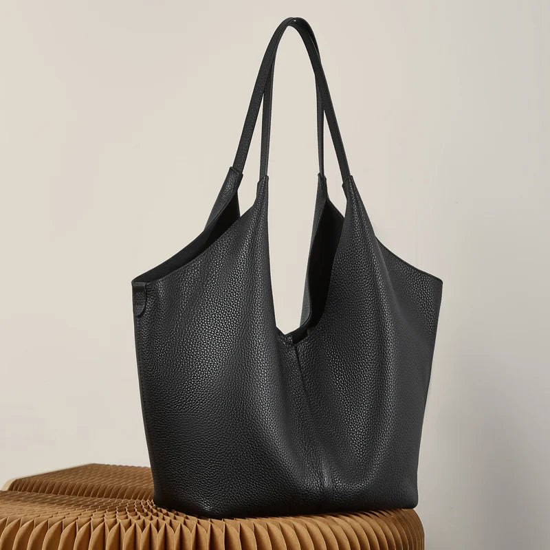 Black pebbled leather tote with an open top, standing against a brown ribbed bench.