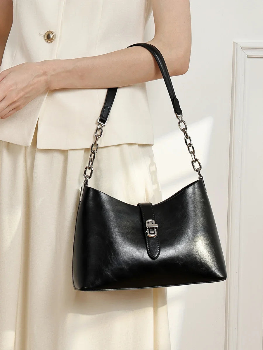 Black leather handbag carried on an arm, showing a smooth surface and chain strap detail