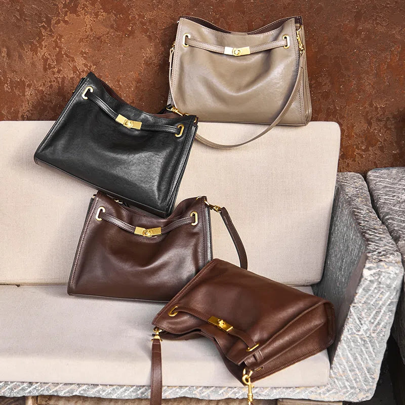 Four Cuirae genuine leather crossbody bags in black, grey, and brown shades resting together on a light-colored sofa.