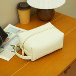 Cuirae beige pebbled leather makeup bag on wooden nightstand, still life with newspaper and coffee cup
