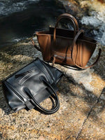 The Cuirae black and brown genuine leather handbags resting on a rock near a stream.