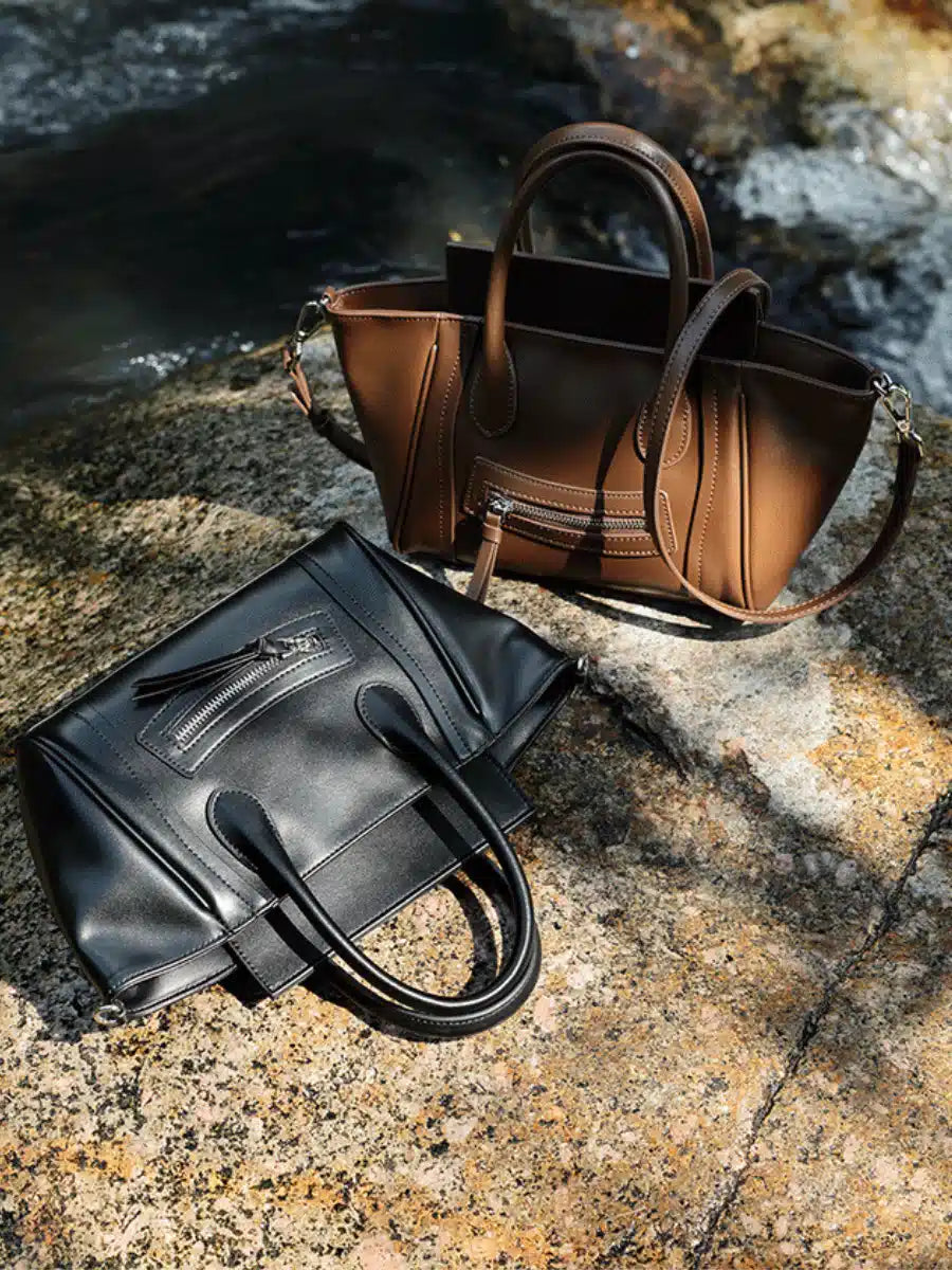 The Cuirae black and brown genuine leather handbags resting on a rock near a stream.