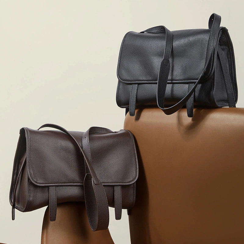 Two Cuirae genuine leather shoulder bags in black and brown resting on a chair.