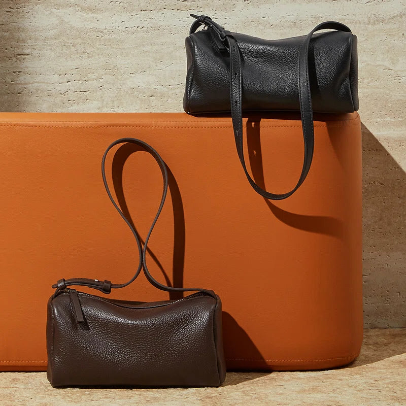 Two Cuirae top grain cowhide crossbody bags in black and brown colors resting on and against an orange leather bench.