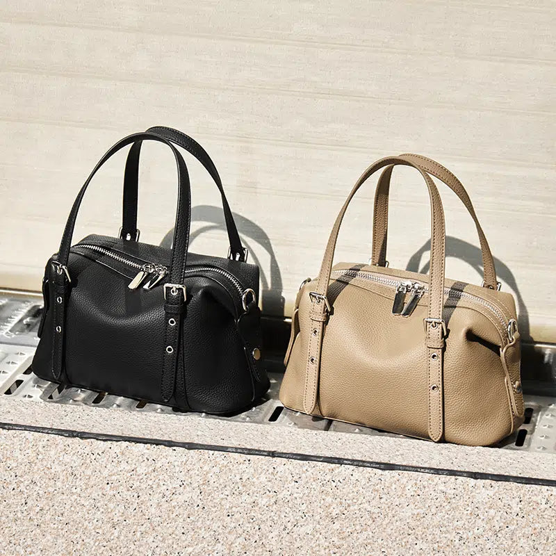 Two Cuirae top grain cowhide shoulder bags in black and tan sitting outside in the sun.