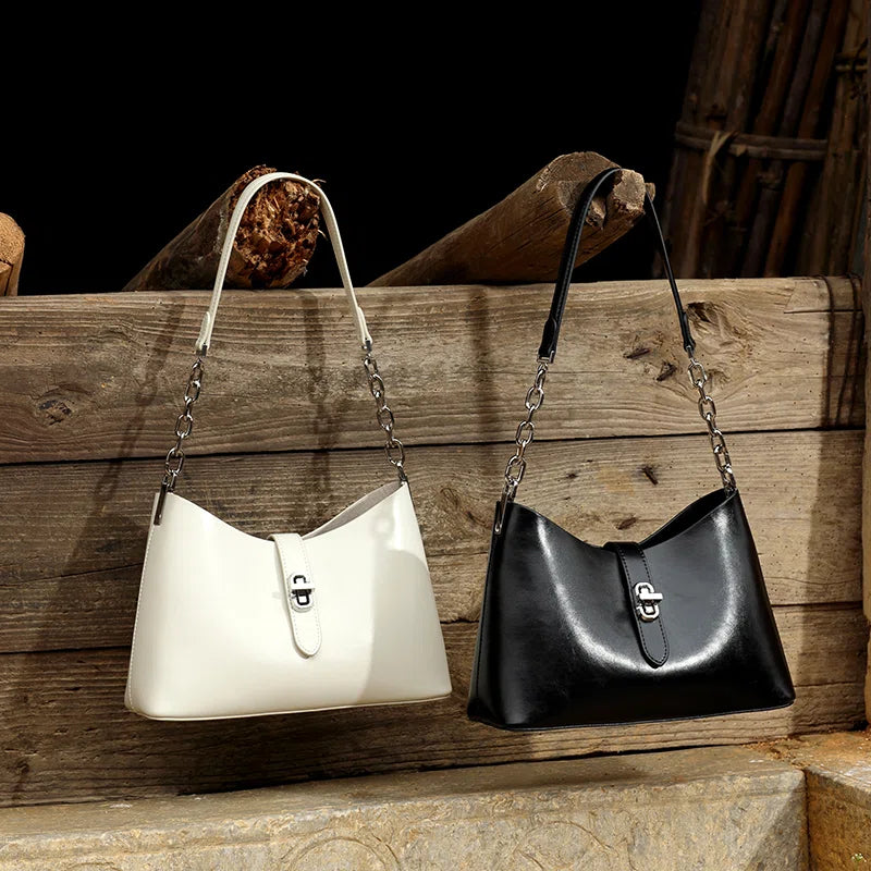 Two Cuirae top grain cowhide handbags in black and white hanging on a wooden fence.