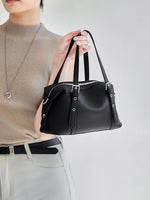 Woman holding Cuirae black genuine leather bowling bag by top handles, front view showing pebbled leather texture