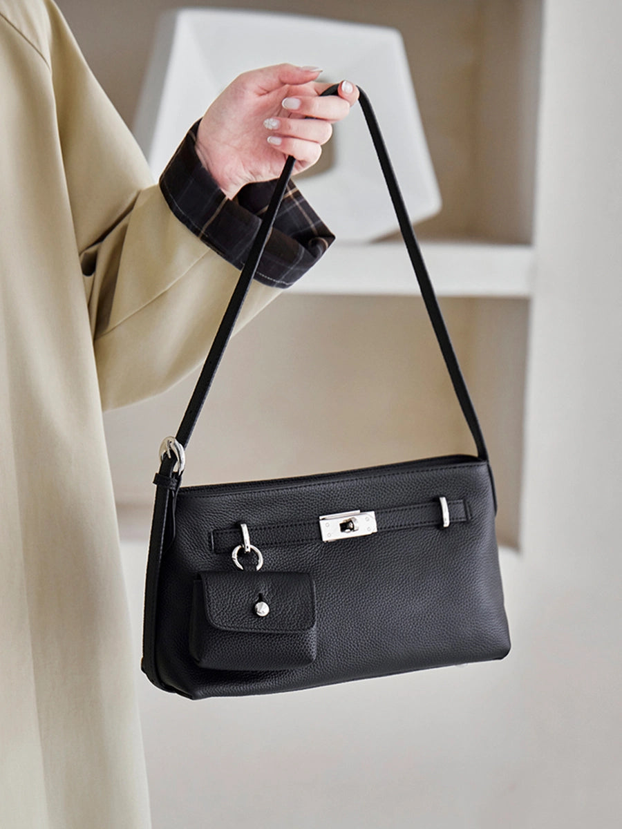 Model holding Cuirae black genuine leather crossbody bag by strap, front view showcasing pebbled texture and coin purse