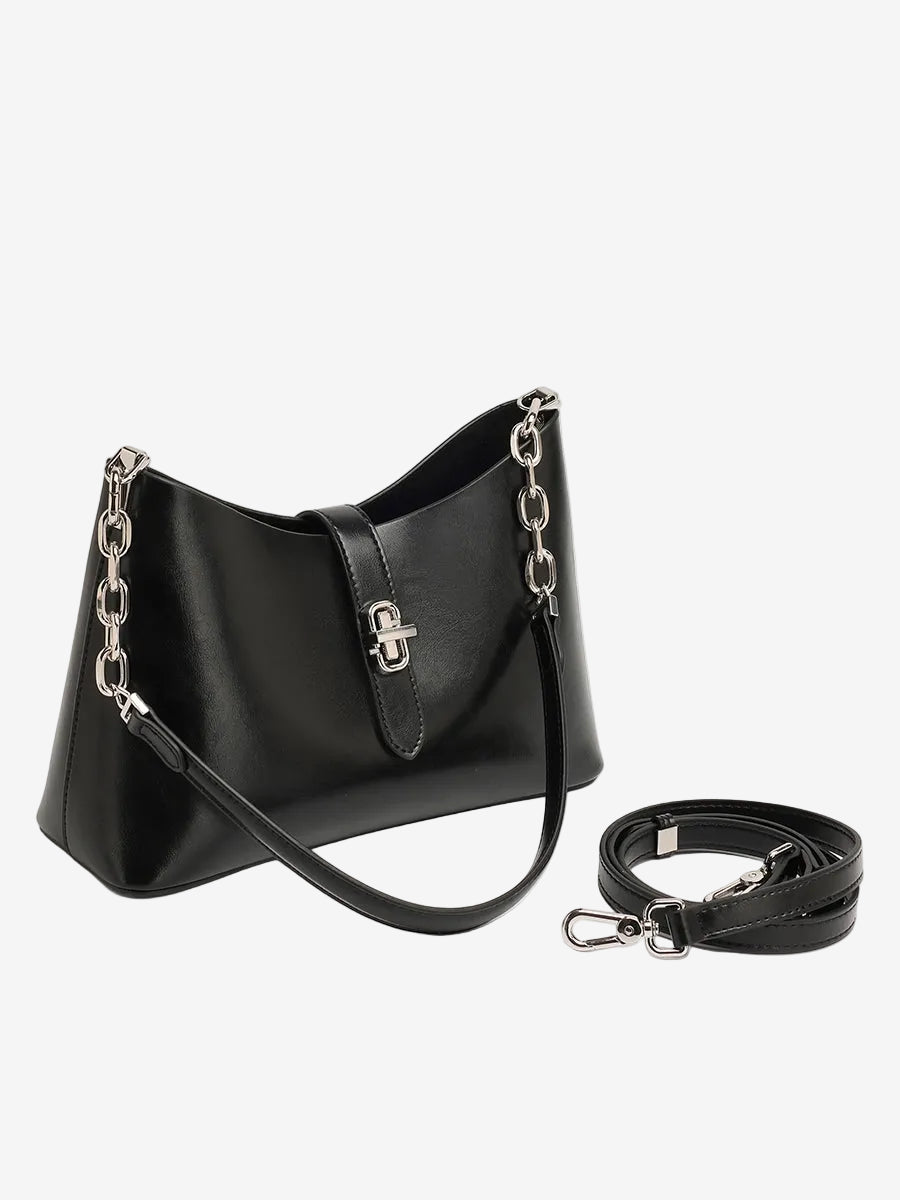 The Cuirae black genuine leather handbag sitting next to an extra long strap on a white background.