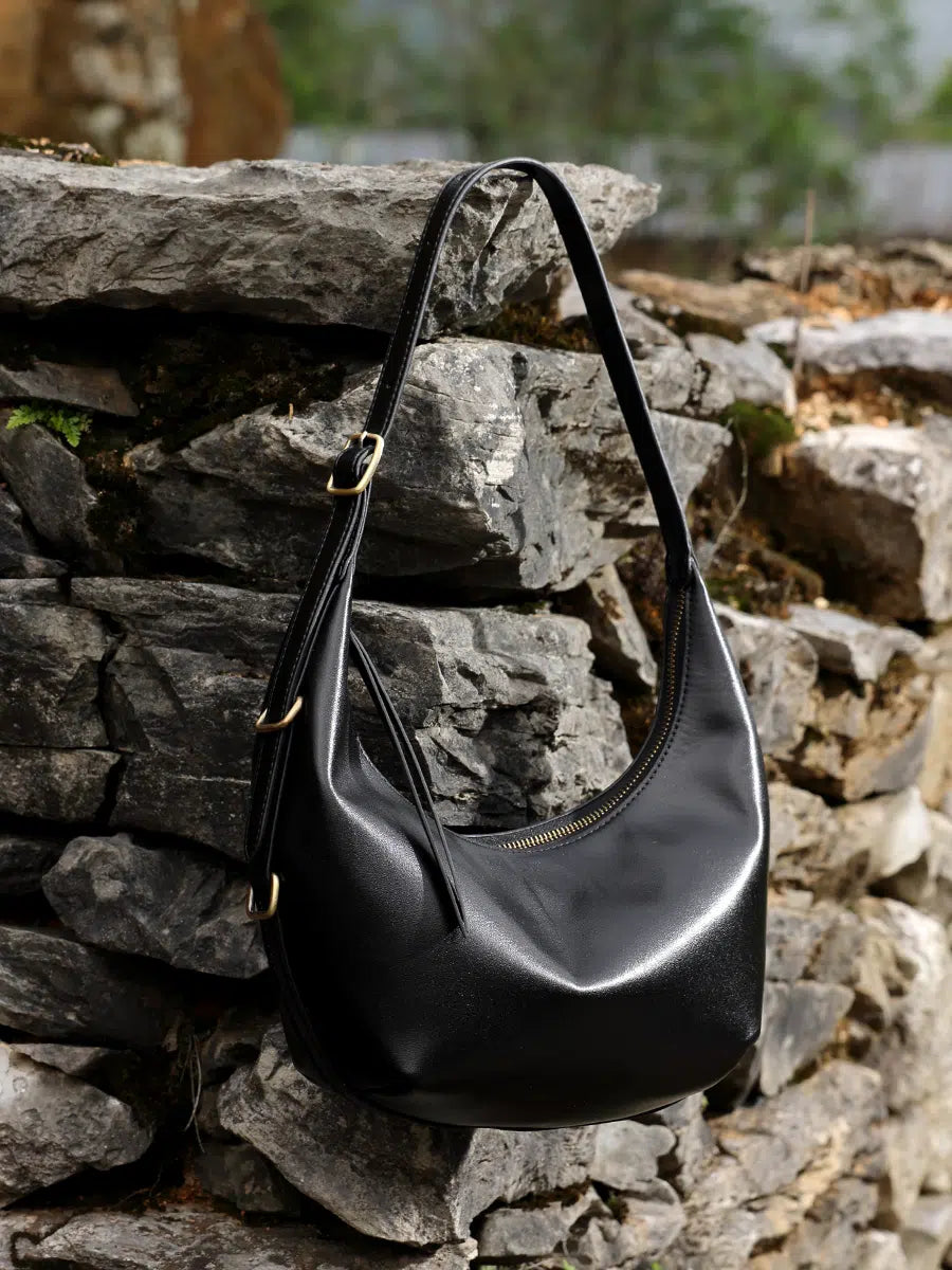 A Cuirae black genuine leather handbag hanging on a stone wall outside.