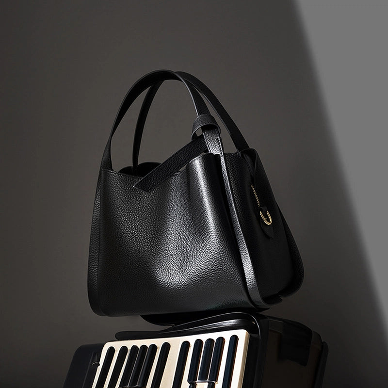 A Cuirae black genuine leather handbag sitting on top of a piano keyboard against a grey background.