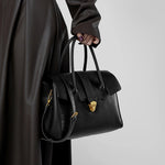 Cuirae black genuine leather satchel bag for women with gold lock hardware and detachable shoulder strap, handheld closeup view