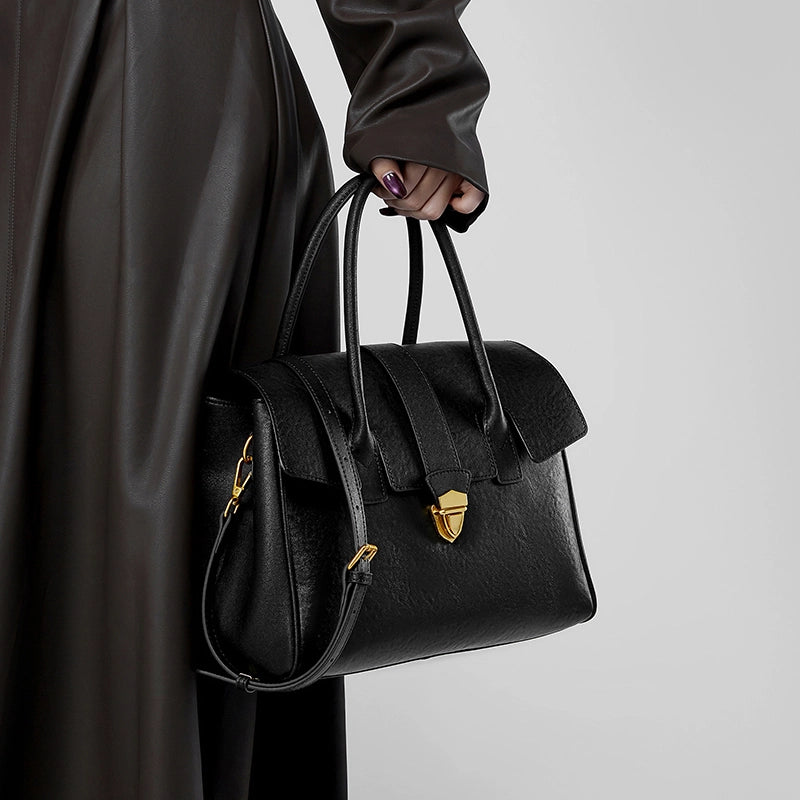 Cuirae black genuine leather satchel bag for women with gold lock hardware and detachable shoulder strap, handheld closeup view