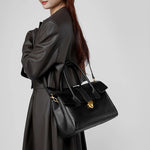 Woman wearing Cuirae black genuine leather satchel bag crossbody style, side view with gold hardware details