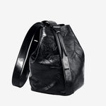 Cuirae black glossy crinkled genuine leather bucket bag with wide shoulder strap, front angled view on white background