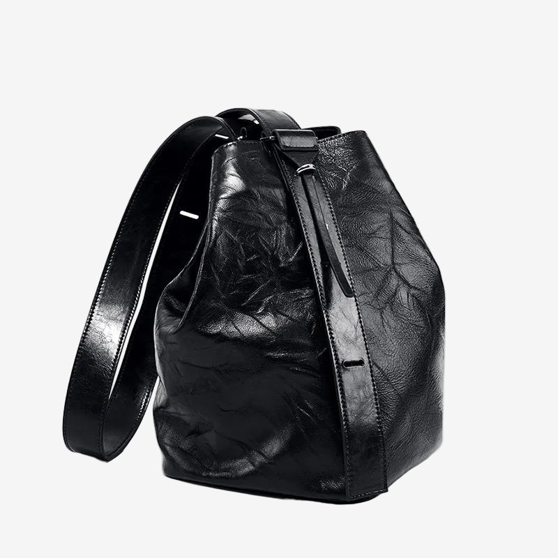 Cuirae black glossy crinkled genuine leather bucket bag with wide shoulder strap, front angled view on white background