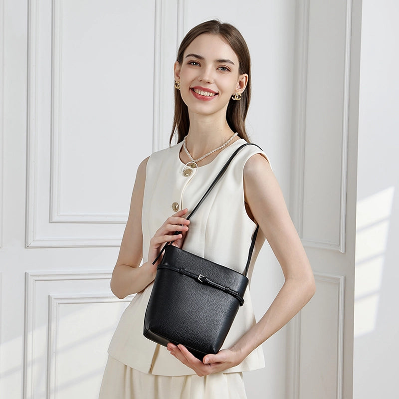 Model wearing Cuirae black leather bucket bag crossbody, front view with white sleeveless vest outfit