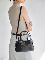 Model wearing Cuirae black pebbled genuine leather bowling bag crossbody, back view showing detachable shoulder strap and silver hardware