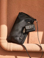 Cuirae black pebbled leather crossbody bag with detachable coin purse on terracotta surface, angled view showing silver turnlock