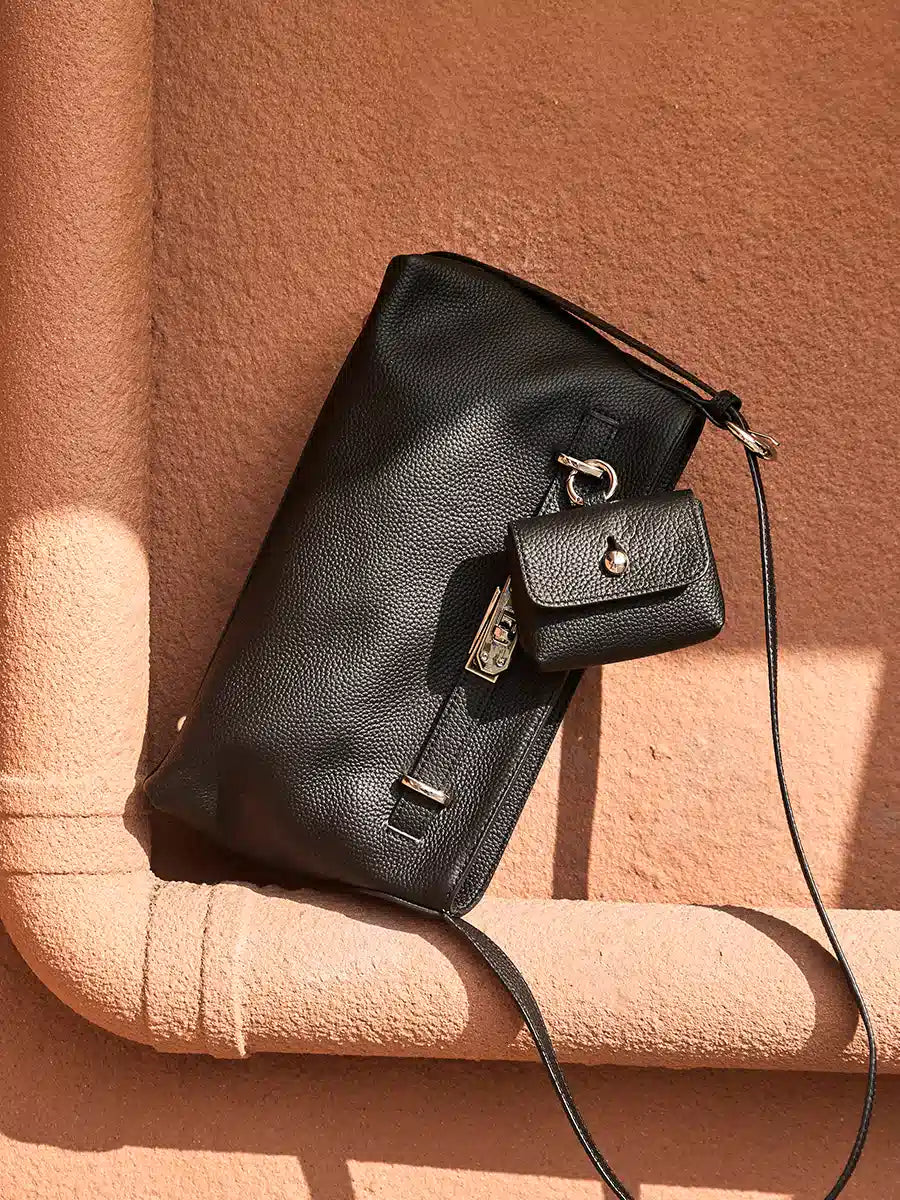 Cuirae black pebbled leather crossbody bag with detachable coin purse on terracotta surface, angled view showing silver turnlock