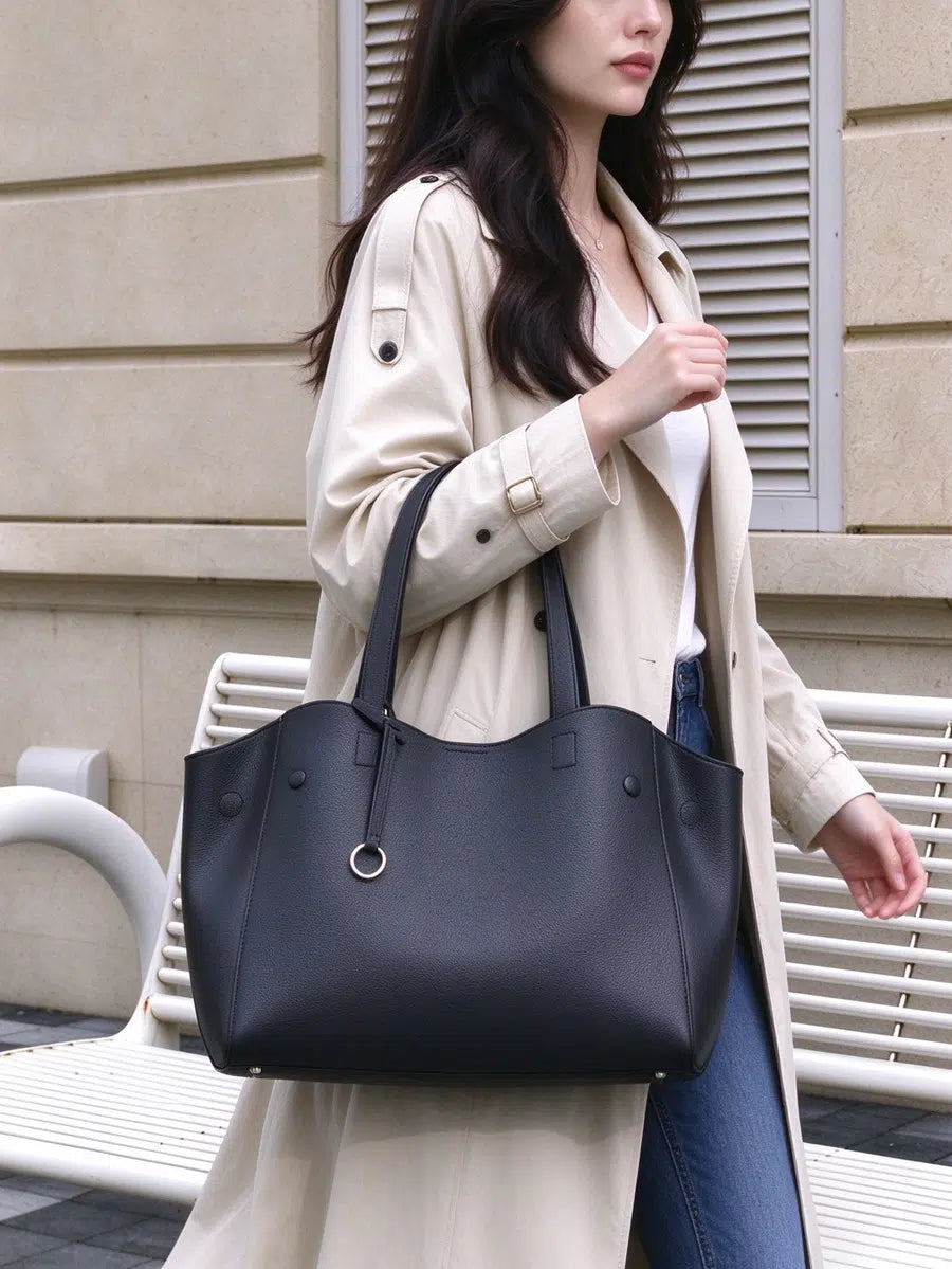 Angled view of a model carrying Cuirae black pebbled genuine leather tote bag on her forearm, showing its side panel and silver ring charm