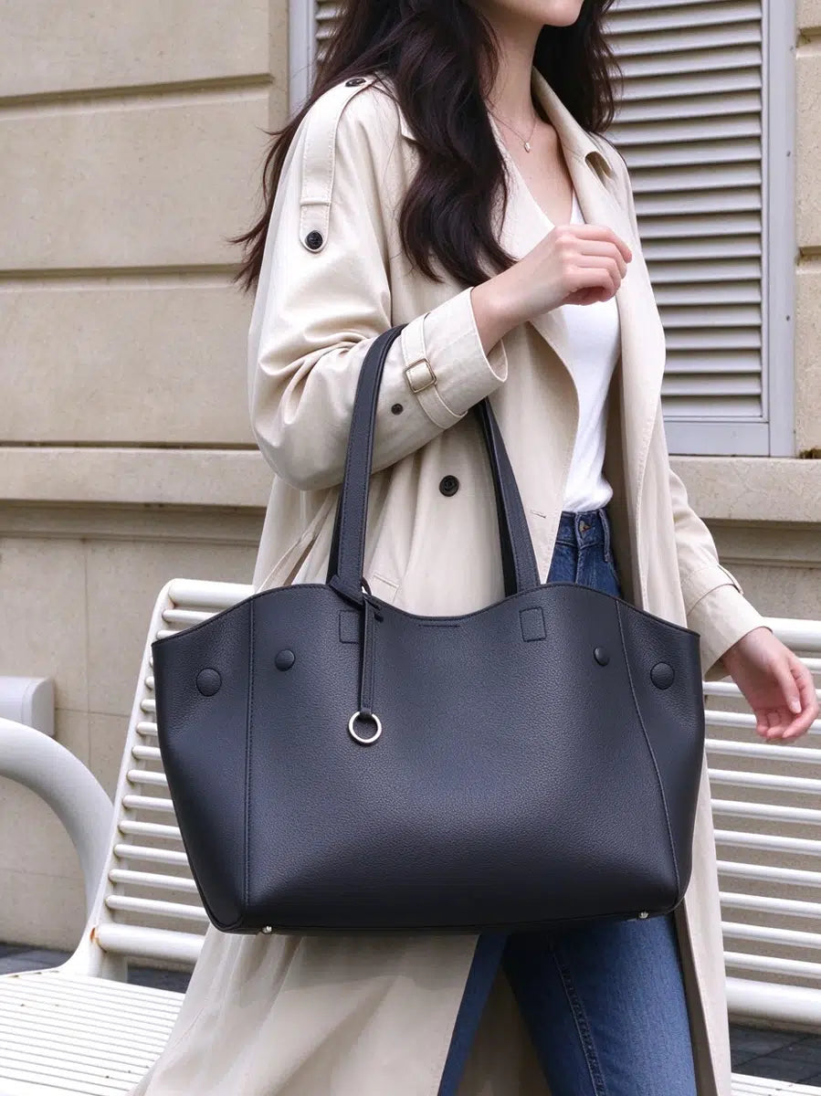 Close view of Cuirae black pebbled genuine leather tote bag carried on a model's forearm, showing long handles and silver ring charm