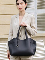 Model holding Cuirae black pebbled genuine leather tote bag by its long handles, front view showing silver ring charm
