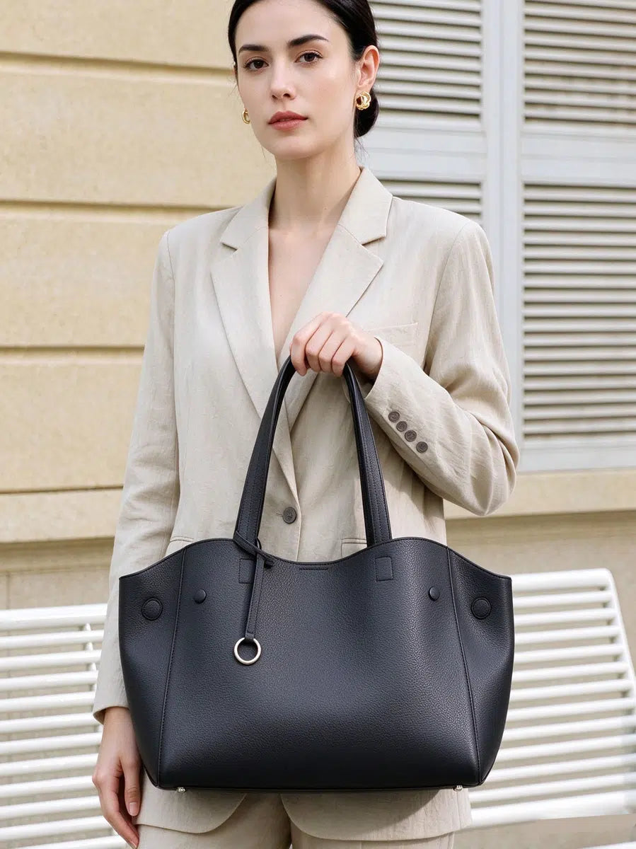 Model holding Cuirae black pebbled genuine leather tote bag by its long handles, front view showing silver ring charm