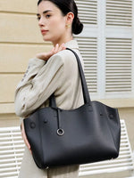 Model wearing Cuirae black pebbled genuine leather tote bag on shoulder, styled with a beige suit