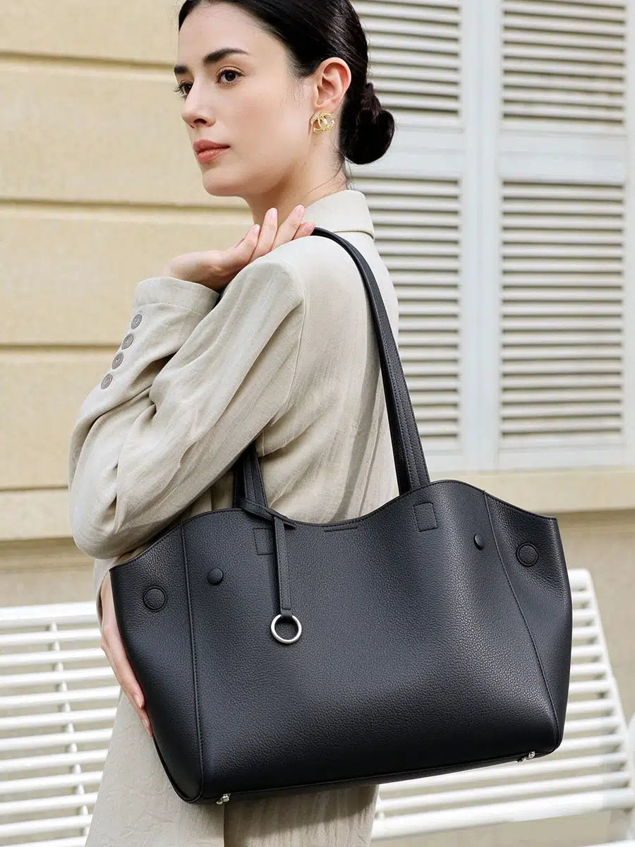 Model wearing Cuirae black pebbled genuine leather tote bag on shoulder, styled with a beige suit