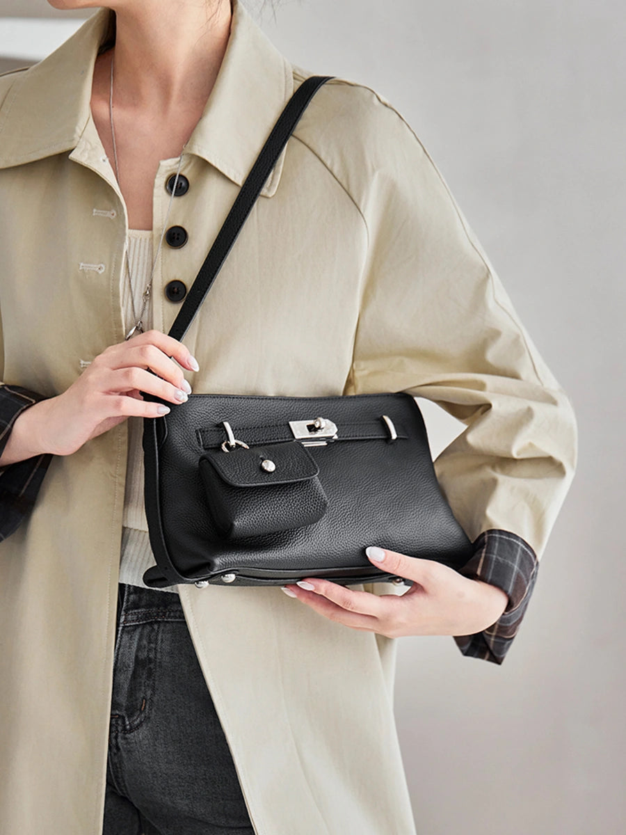 Closeup of model holding Cuirae black pebbled leather crossbody bag, showing detachable coin purse and silver hardware