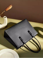 Black pebbled leather tote displayed on its side, showing its rectangular shape and top handles