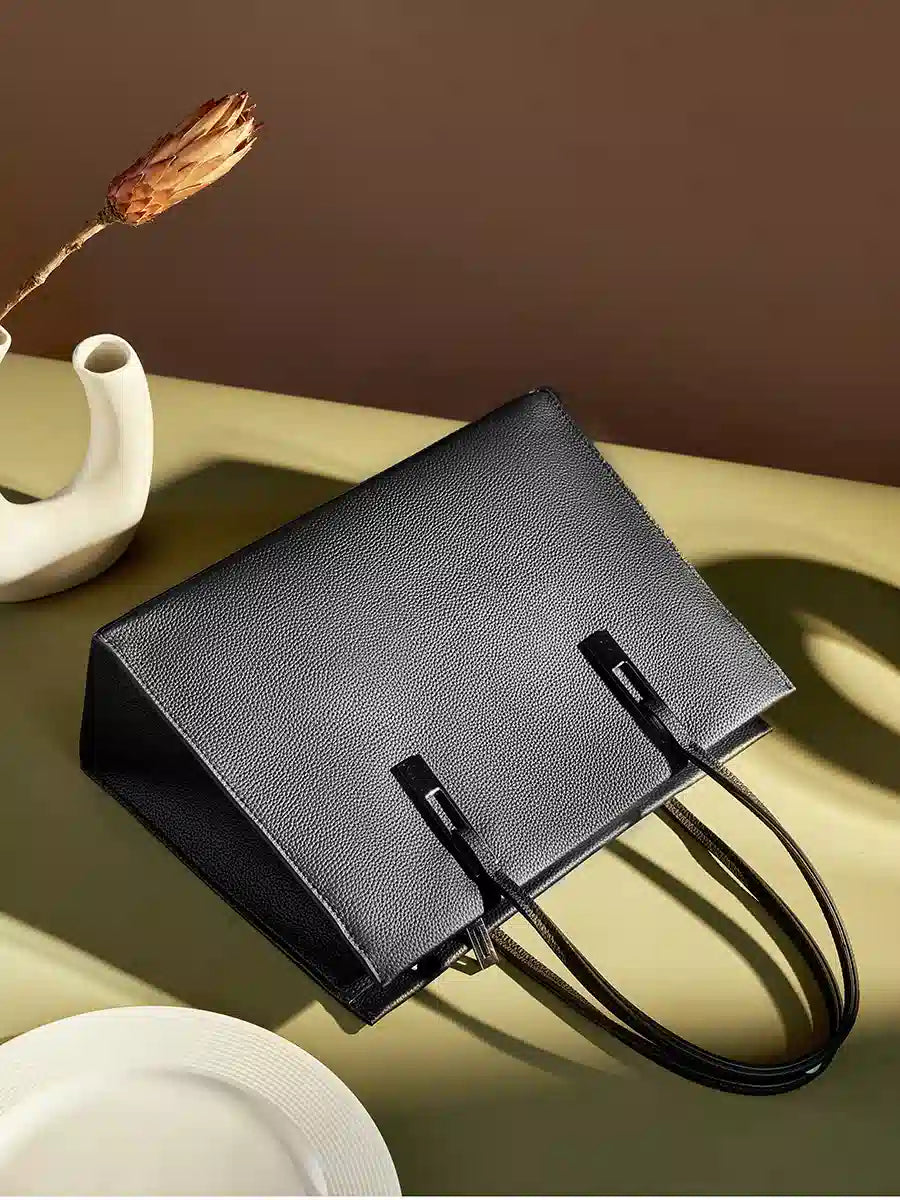 Black pebbled leather tote displayed on its side, showing its rectangular shape and top handles
