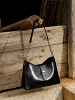 A Cuirae black top grain cowhide handbag hanging on a piece of wood outside.