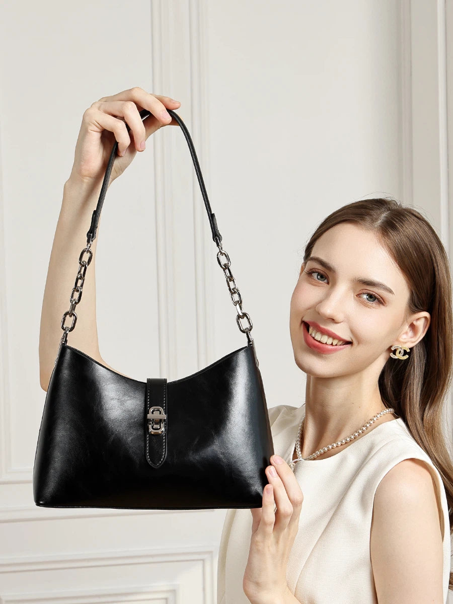 A smiling woman in white holding up the Cuirae black top grain cowhide handbag by its strap.