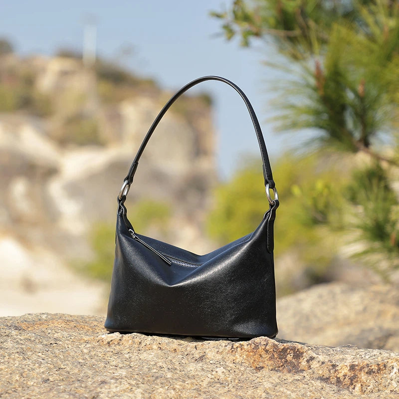 A Cuirae black top grain cowhide shoulder bag resting on a rock outside.