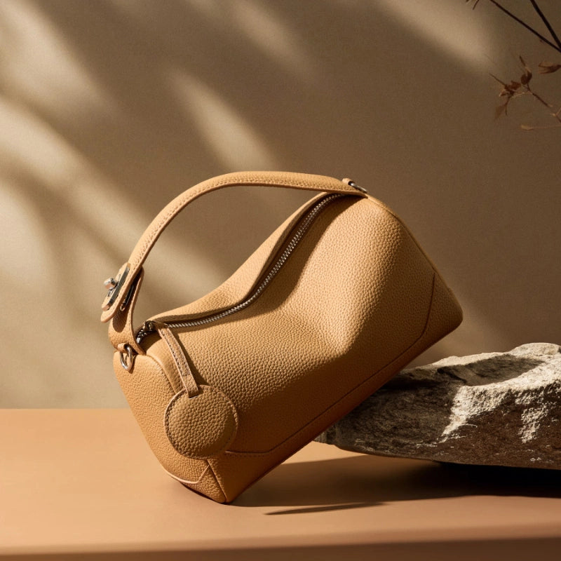Cuirae bronze genuine leather top handle bag angled on stone, showing structured silhouette and zipper closure