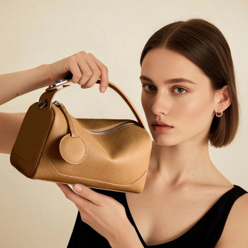 Model holding Cuirae bronze pebbled genuine leather bowling handbag, front view showing round charm and silver hardware
