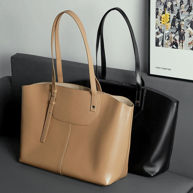 Two Cuirae top grain cowhide handbags in brown and black resting on a grey sofa next to a framed picture.