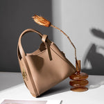 Cuirae brown handbag in minimalist still life with dried flower, natural light showing structured top handle design
