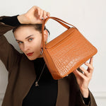 Cuirae brown crocodile embossed genuine leather crossbody bag held by model, closeup showing textured flap and silver hardware